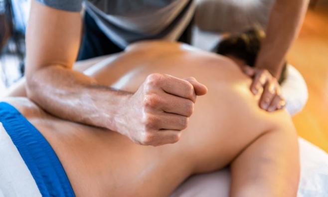 Physiotherapeut gibt Patientin eine Massage des Rückens mit seinem rechten Unterarm